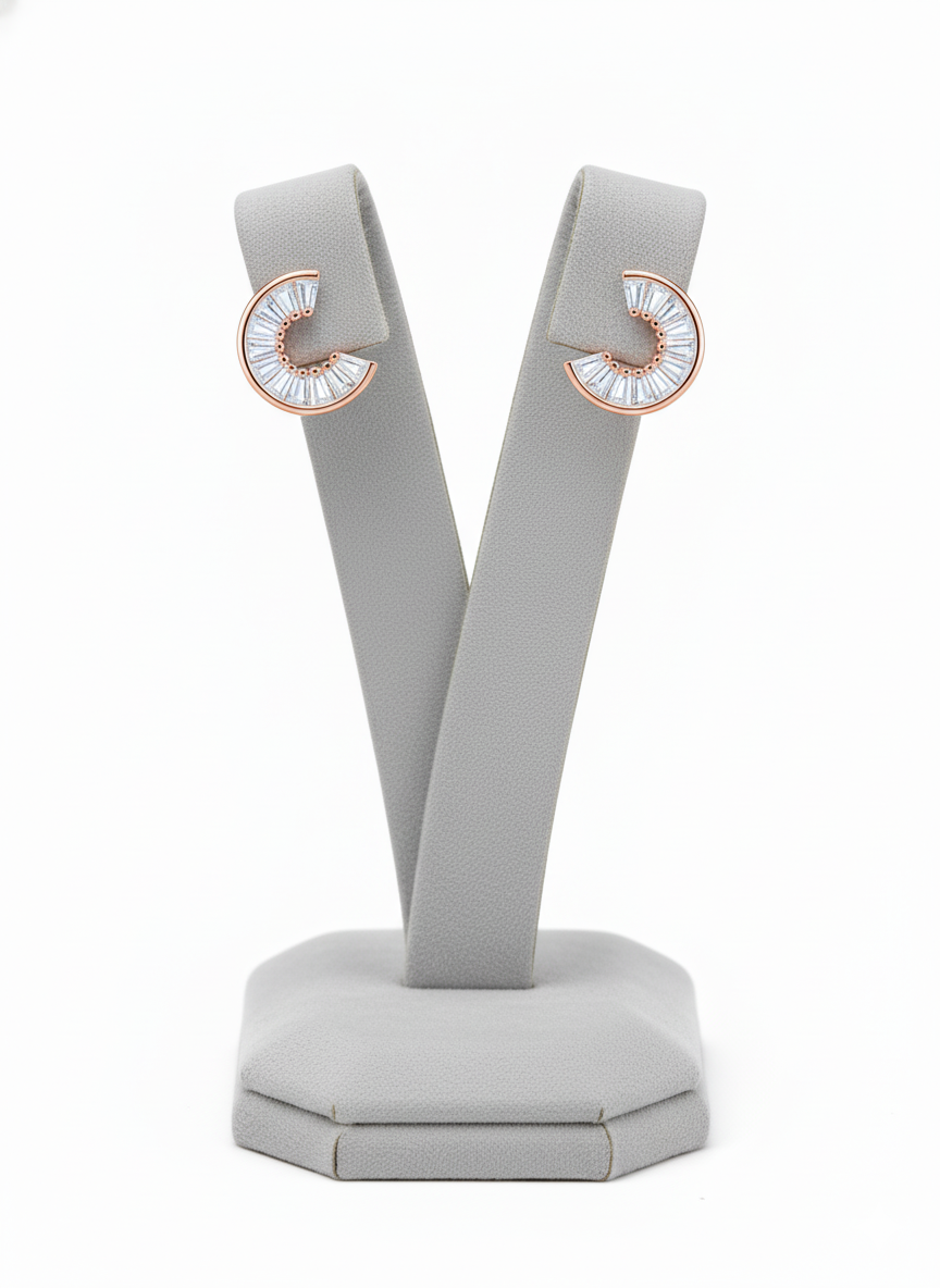 Rohari crescent stud earrings in rose gold, featuring baguette American diamonds, displayed on a gray jewelry stand.