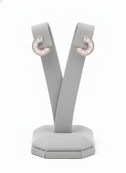 Rohari crescent stud earrings in rose gold, featuring baguette American diamonds, displayed on a gray jewelry stand.