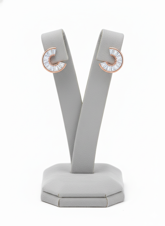Rohari crescent stud earrings in rose gold, featuring baguette American diamonds, displayed on a gray jewelry stand.
